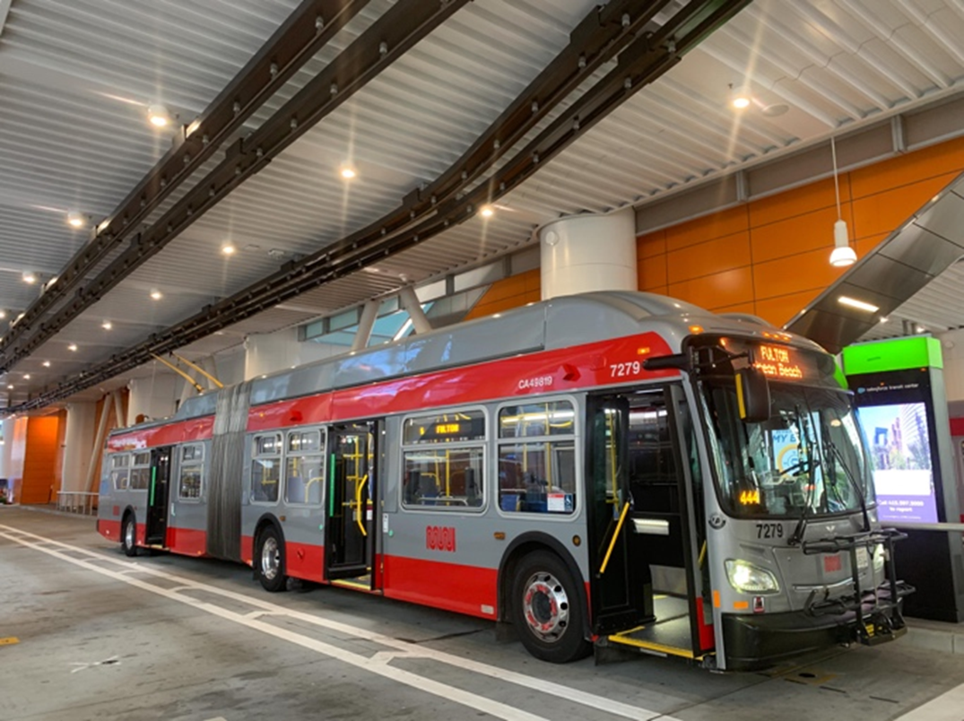 Image shows an articulated municipal bus waiting at the Salesforce Transit Center.