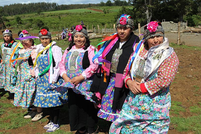 Mujeres mapuches con vestidos floridos y tocados con flores.