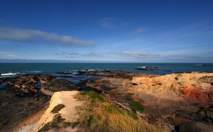 Photograph of a rocky beach leading to the ocean with a blue sky abovev