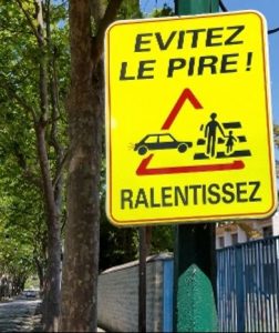 A yellow traffic sign reading "Évitez le pire! Ralentissez!" (Avoid the worst! Slow down!)