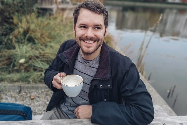 young man with brown hair and mustache drinking coffee