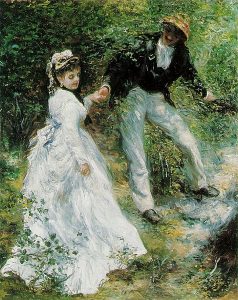 A young man holds the hand of a young woman as they walk through a park