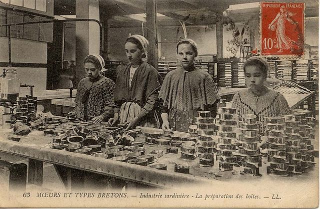 4 young women or adolescents in caps and shawls prepare cans for sardines